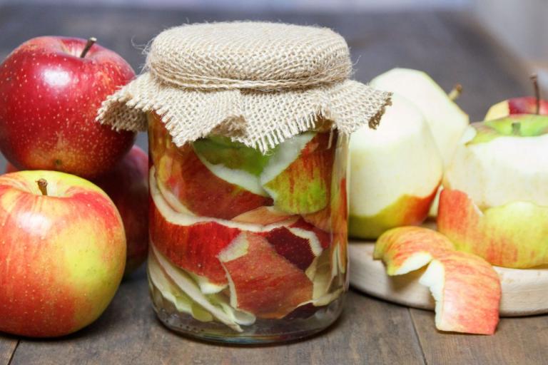 Jar of apple scrap vinegar surrounded by apples.