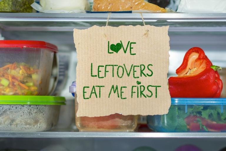 Fridge shelf of plastic containers with a sign reading Love leftovers, eat me first.