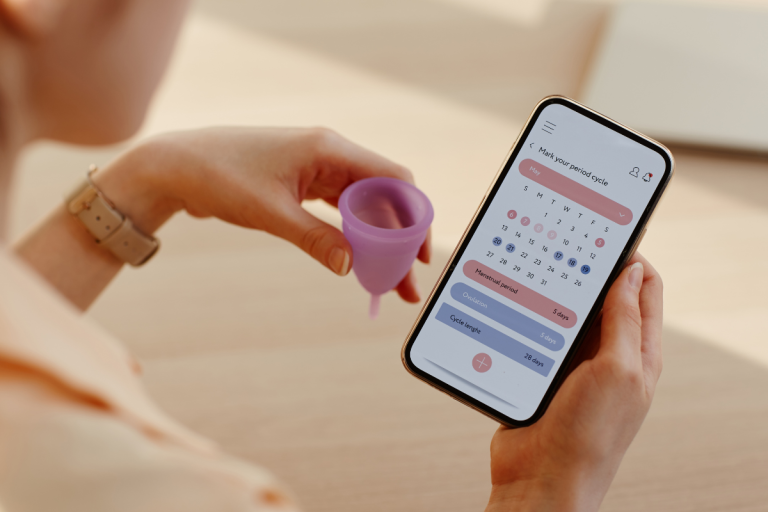 Person holding menstrual cup and looking at period tracker on mobile phone.