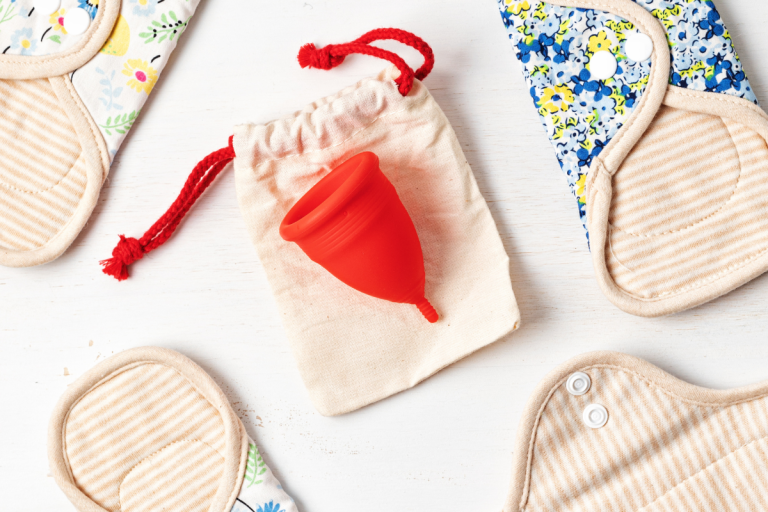 Selection of reusable period pads surrounding a red menstrual cup.