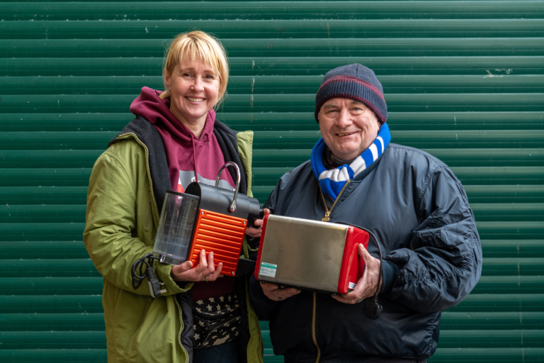Two people holding coffee machine and toaster.