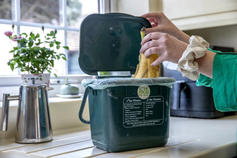 Hand placing a banana skin in a food recycling caddy.