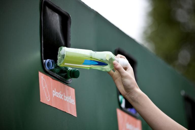 Hand placing a plastic bottle into a recycling bin.