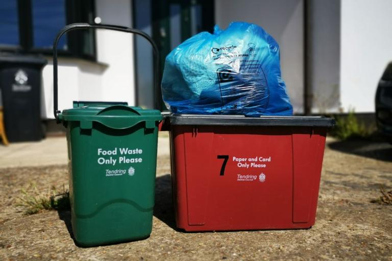 A food waste caddy, recycling box and textile recycling bag on a driveway.