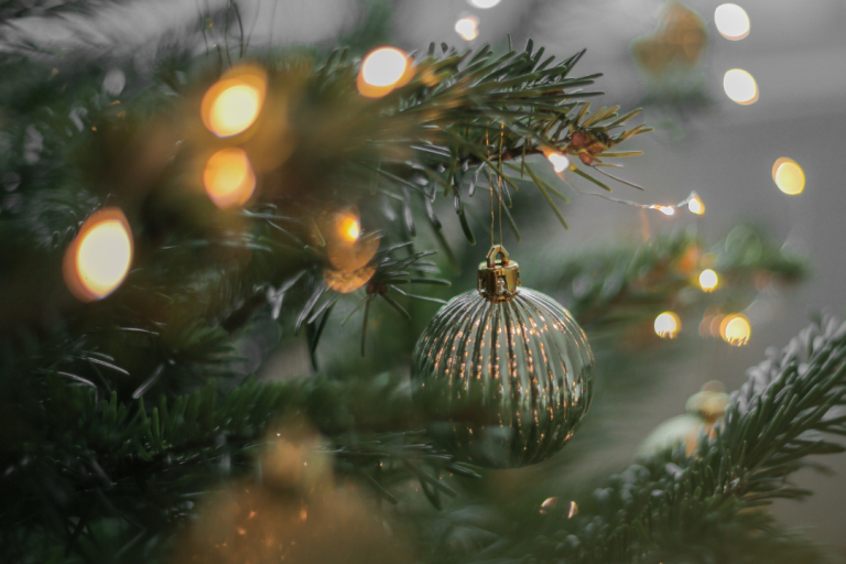 Golden bauble surrounded by Christmas lights on a Christmas tree.