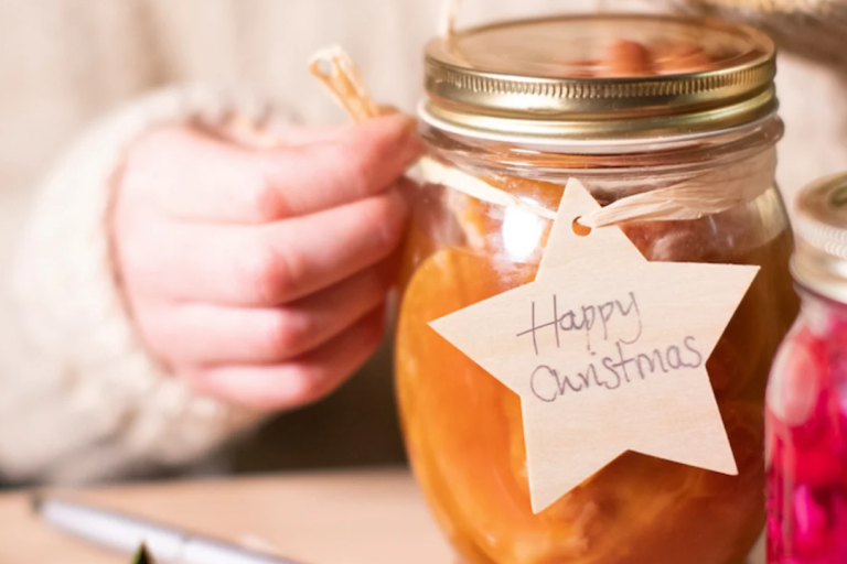 A pair of hands decorating an upcycled glass mason jar with the label "Happy christmas" on it.