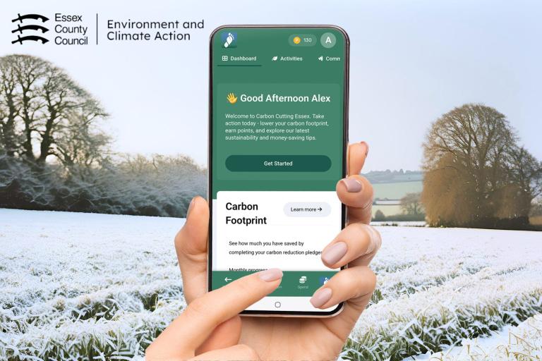 A hand tapping on a phone with the Carbon Cutting Essex app open, with a background of a snowy field.