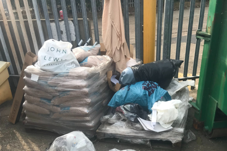 Bags of rubbish outside the railings of a recycling centre.