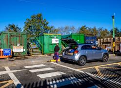 Person next to car with it's boot open at a recycling centre.