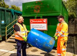 Two recycling centre staff members carrying a large rigid plastic item at a recycling centre.