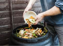 A person adding food waste to a black compost bin