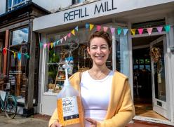 Vicki Daws, founder of Refill Mill, standing outside the shop holding a large soap dispenser. 