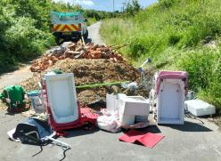 Large fly tip on country lane including rubble, green waste and children’s toys.