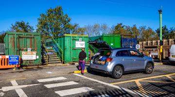 Person next to car with it's boot open at a recycling centre.