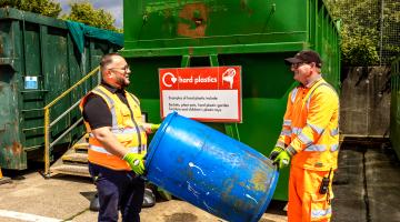 Two recycling centre staff members carrying a large rigid plastic item at a recycling centre