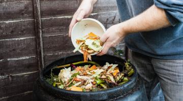 A person adding food waste to a black compost bin