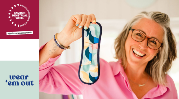 A woman holding a reusable period pad to camera. The Women’s Environmental Network Environmenstrual Week logo is in the top left corner. The Wear Em Out logo is in the bottom left corner.