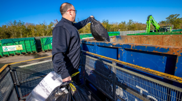 Man putting black ban into a container at a recycling centre