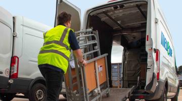 A man wearing a yellow hi-vis vest loading a bed frame onto a van, via a ramp.