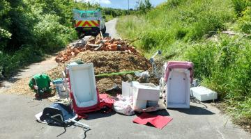 Large fly tip on country lane including rubble, green waste and children’s toys.